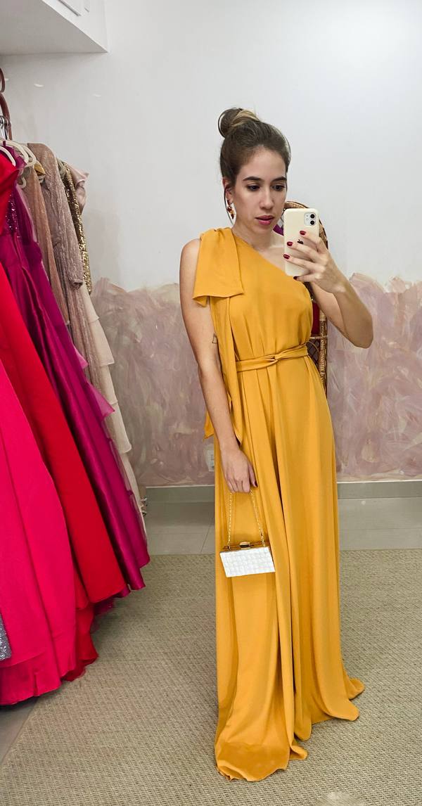 Vestido longo mostarda de decote um ombro com laço decorativo, amarração na cintura e saia fluida.