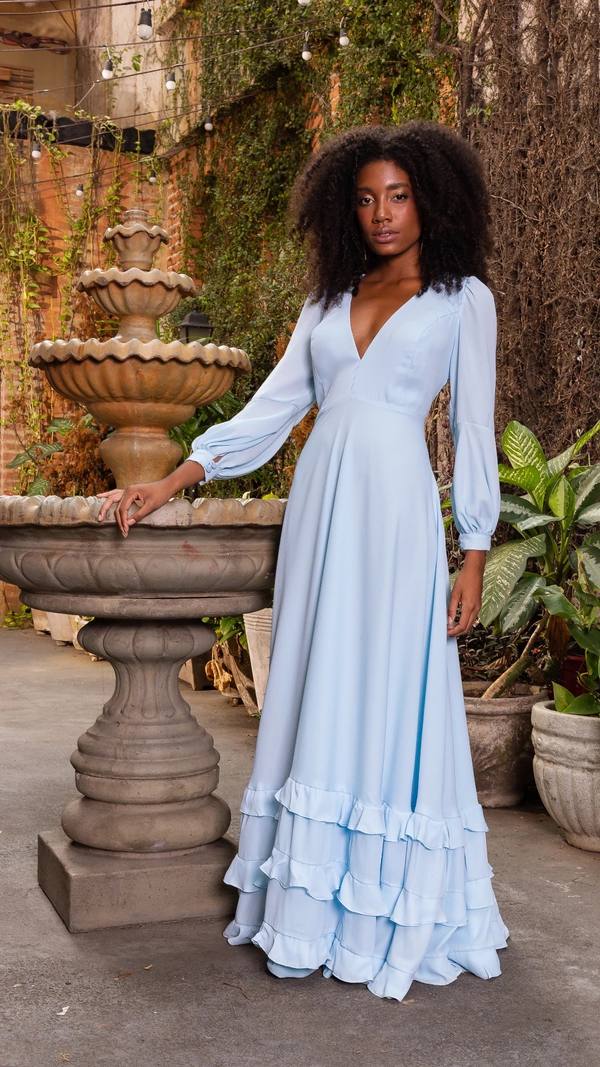 Vestido longo azul claro de tecido fluido, com decote V, mangas longas e saia com babados na barra.