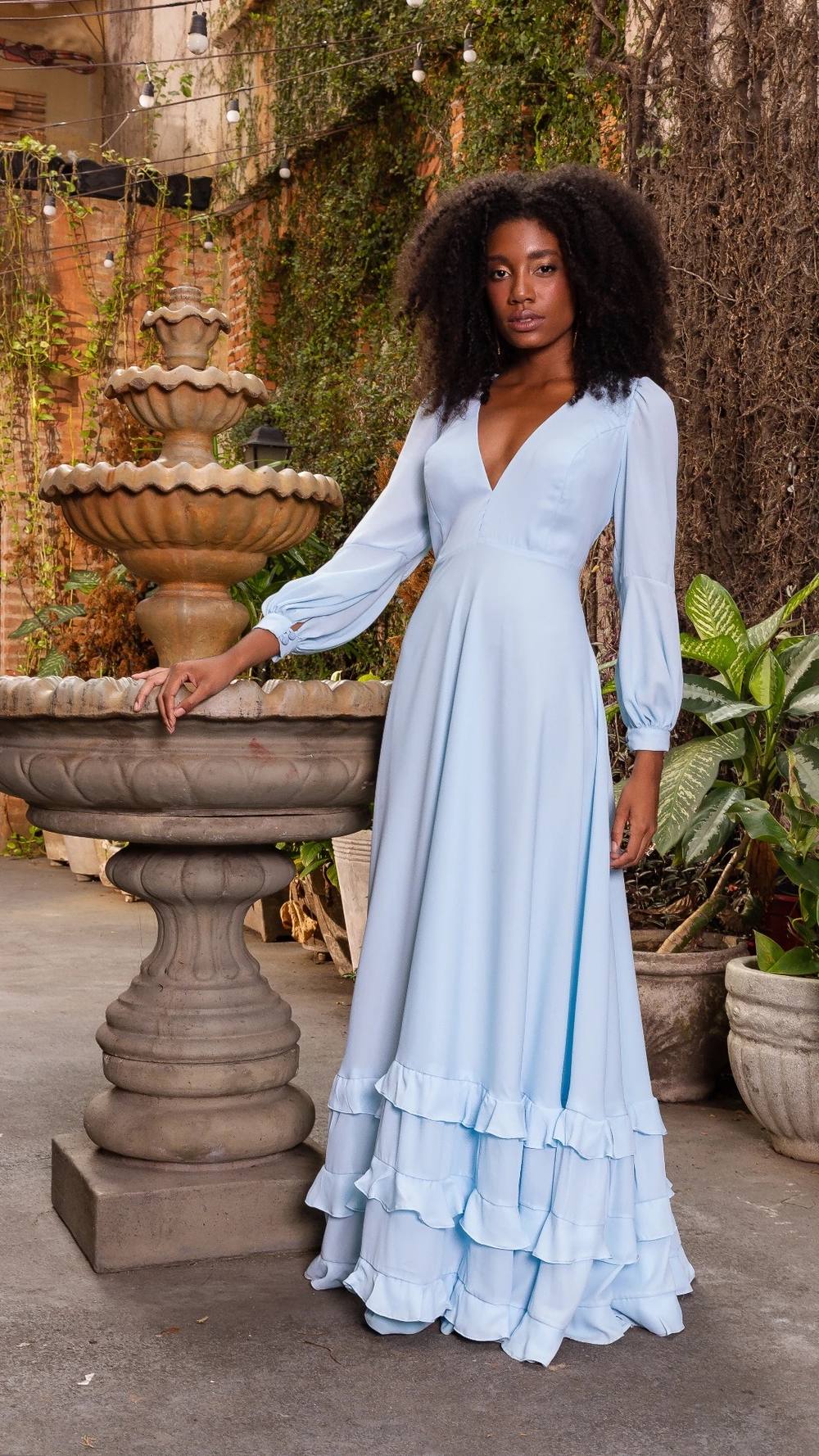 Vestido longo azul claro de tecido fluido, com decote V, mangas longas e saia com babados na barra.