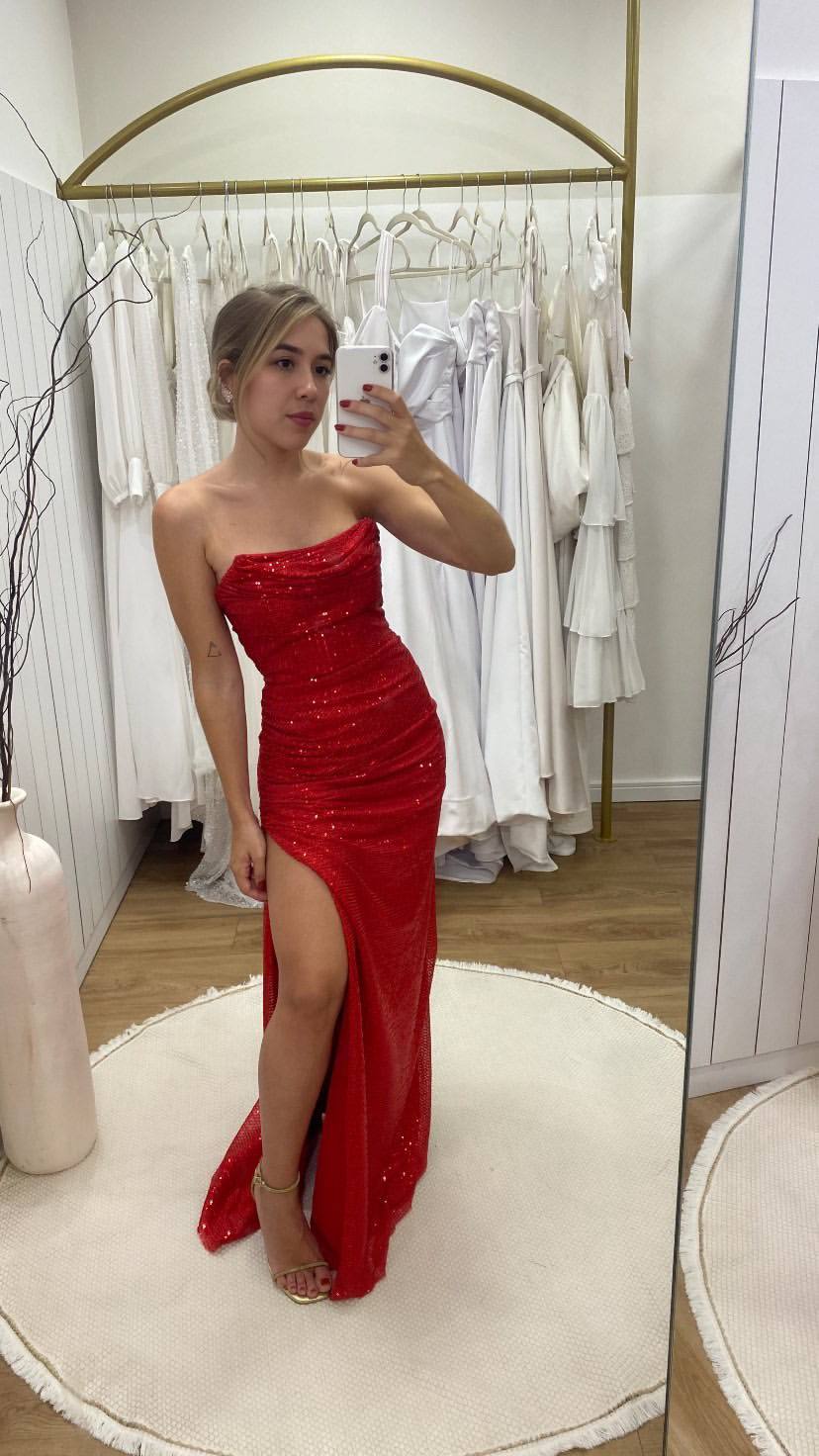 Vestido longo vermelho com paetês, modelagem justa, decote tomara que caia e fenda lateral na saia.