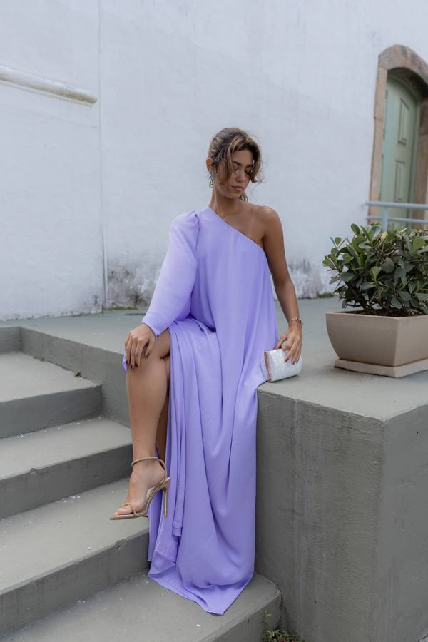 Vestido longo lilás de caimento fluido, modelo um ombro com manga longa e fenda lateral.
