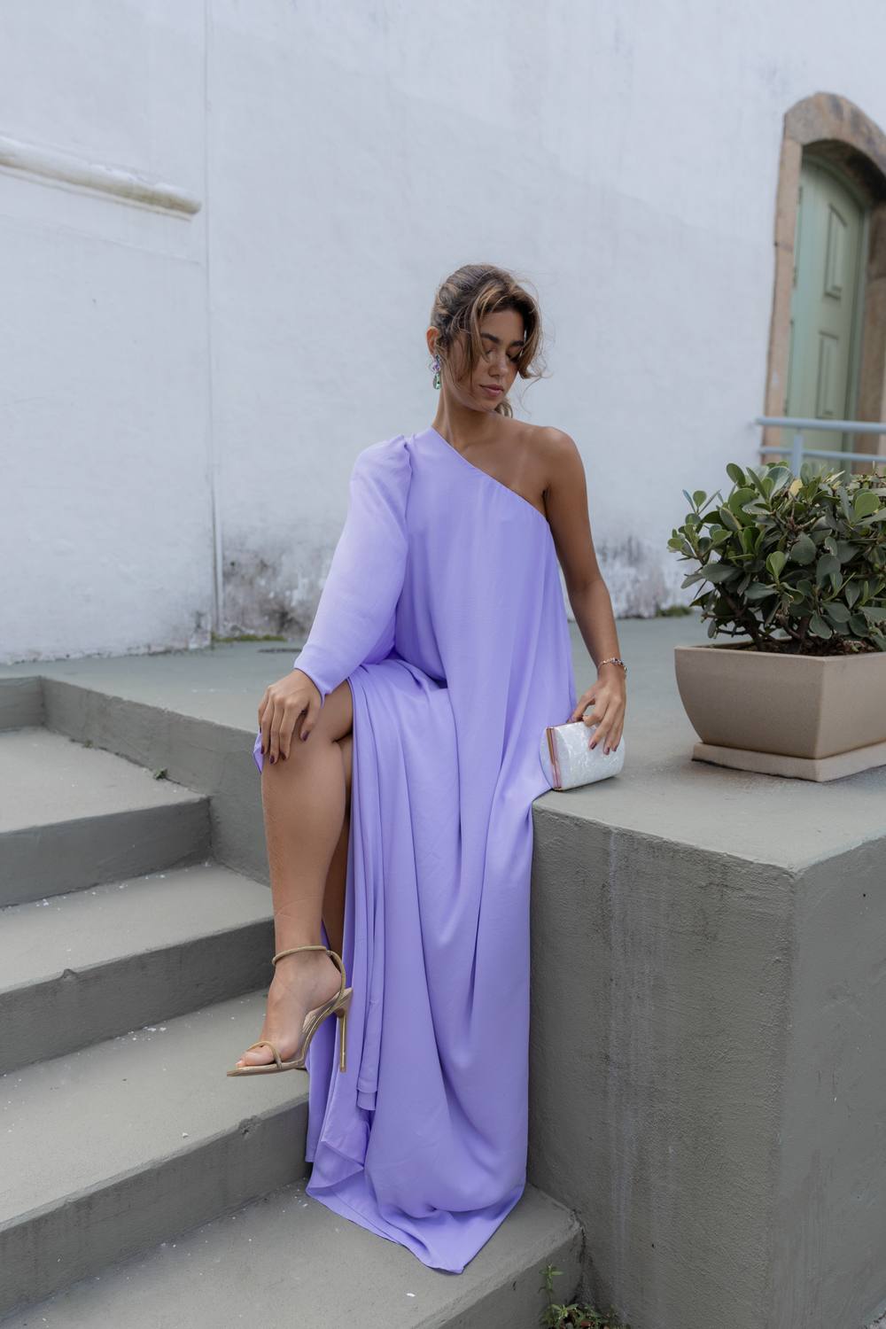 Vestido longo lilás de caimento fluido, modelo um ombro com manga longa e fenda lateral.