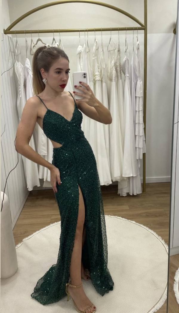 Vestido longo verde escuro com brilho, alças finas, fenda frontal e modelagem ajustada ao corpo.