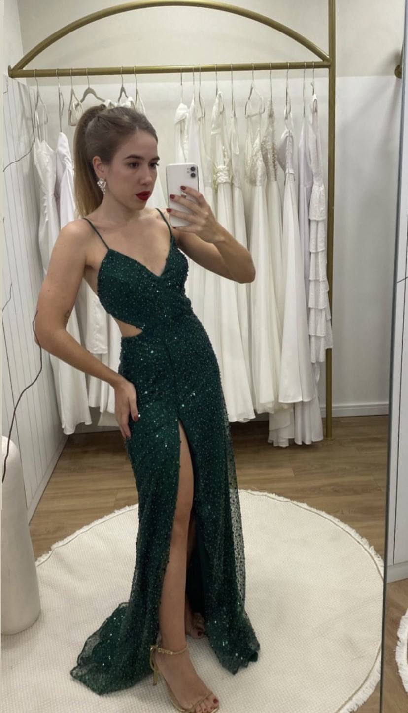 Vestido longo verde escuro com brilho, alças finas, fenda frontal e modelagem ajustada ao corpo.