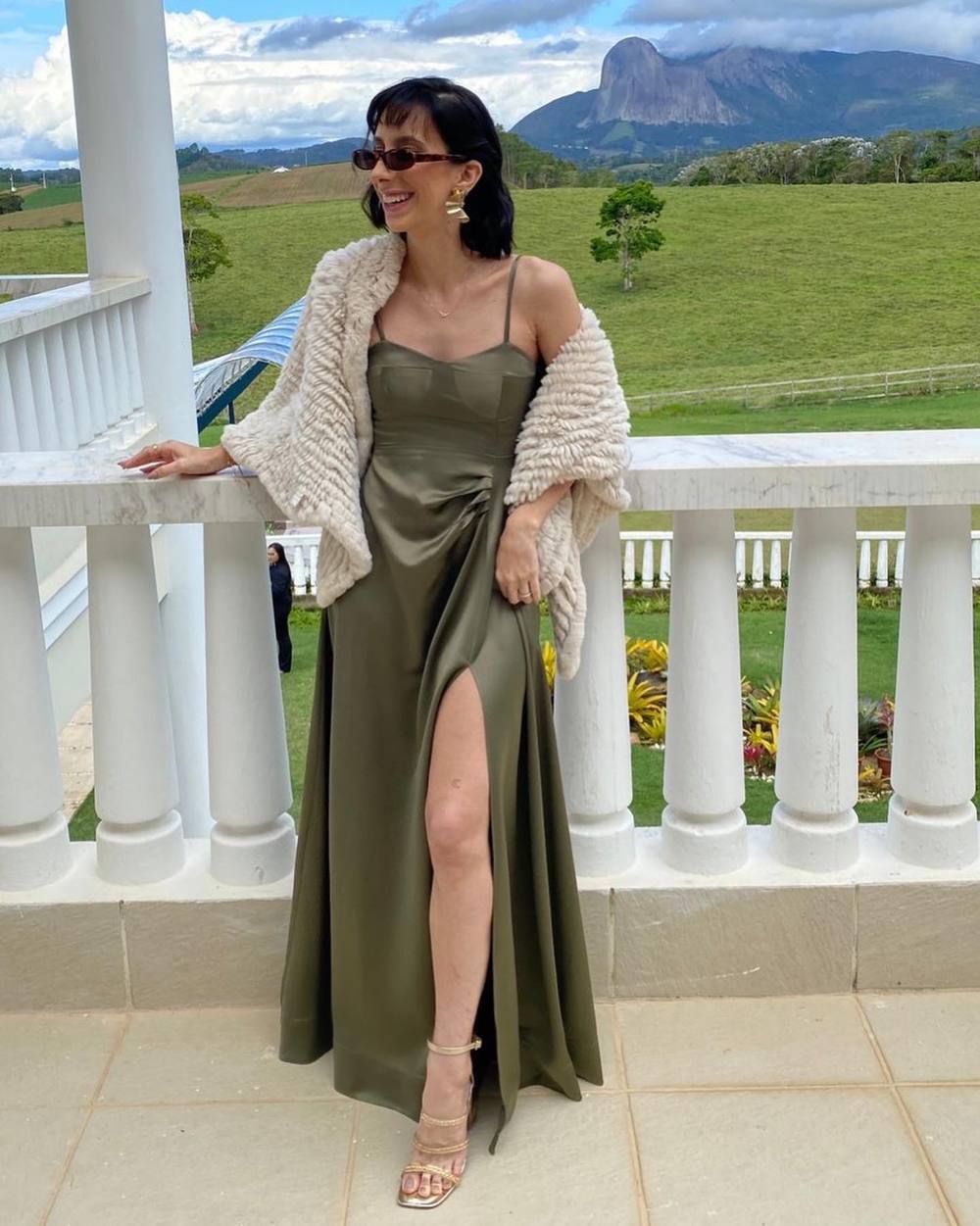 Vestido longo verde oliva de cetim, com alça fina, fenda frontal e caimento fluido.