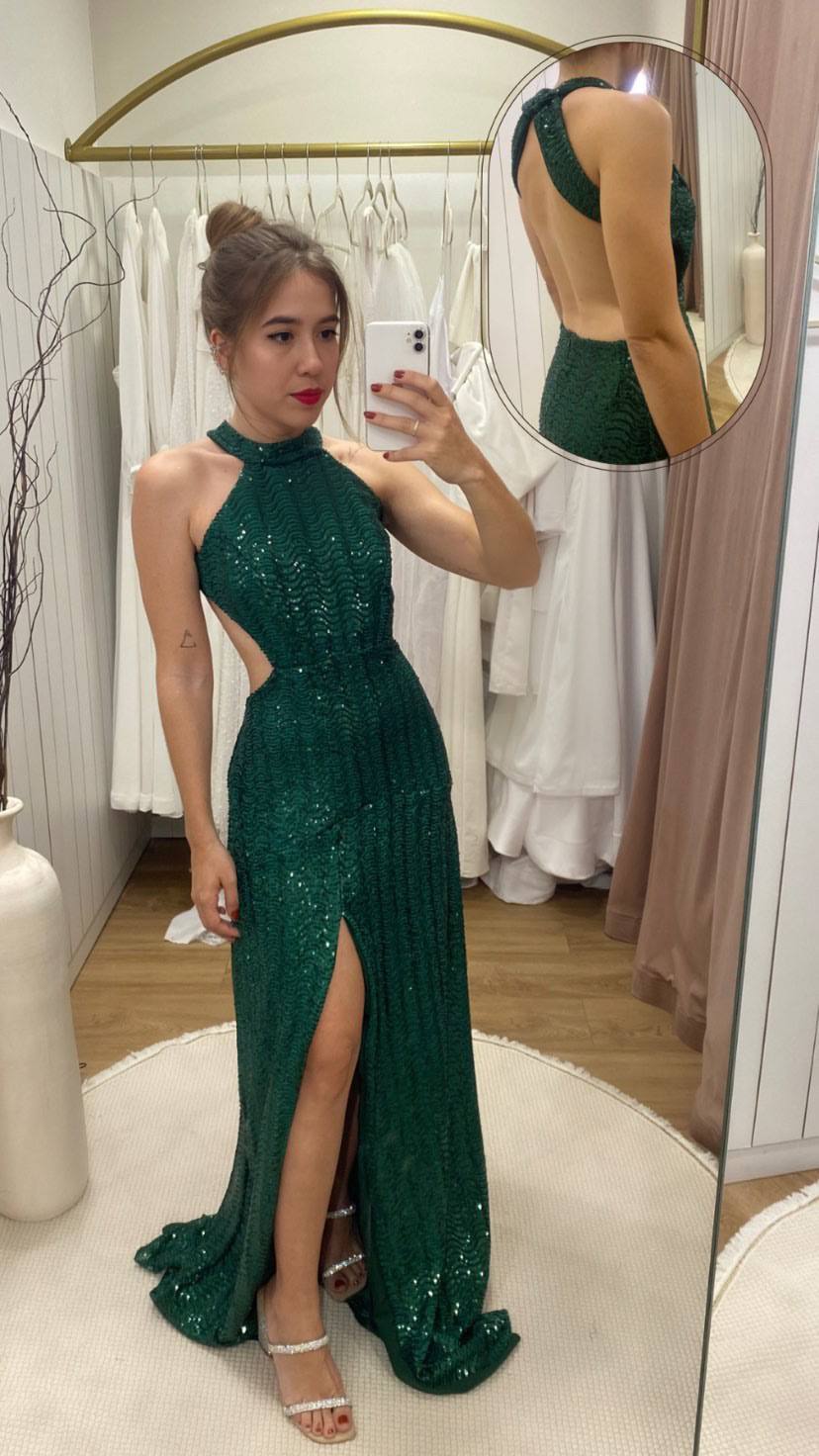 Vestido longo verde de paetês, com decote frente única, costas abertas, caimento reto e fenda frontal.