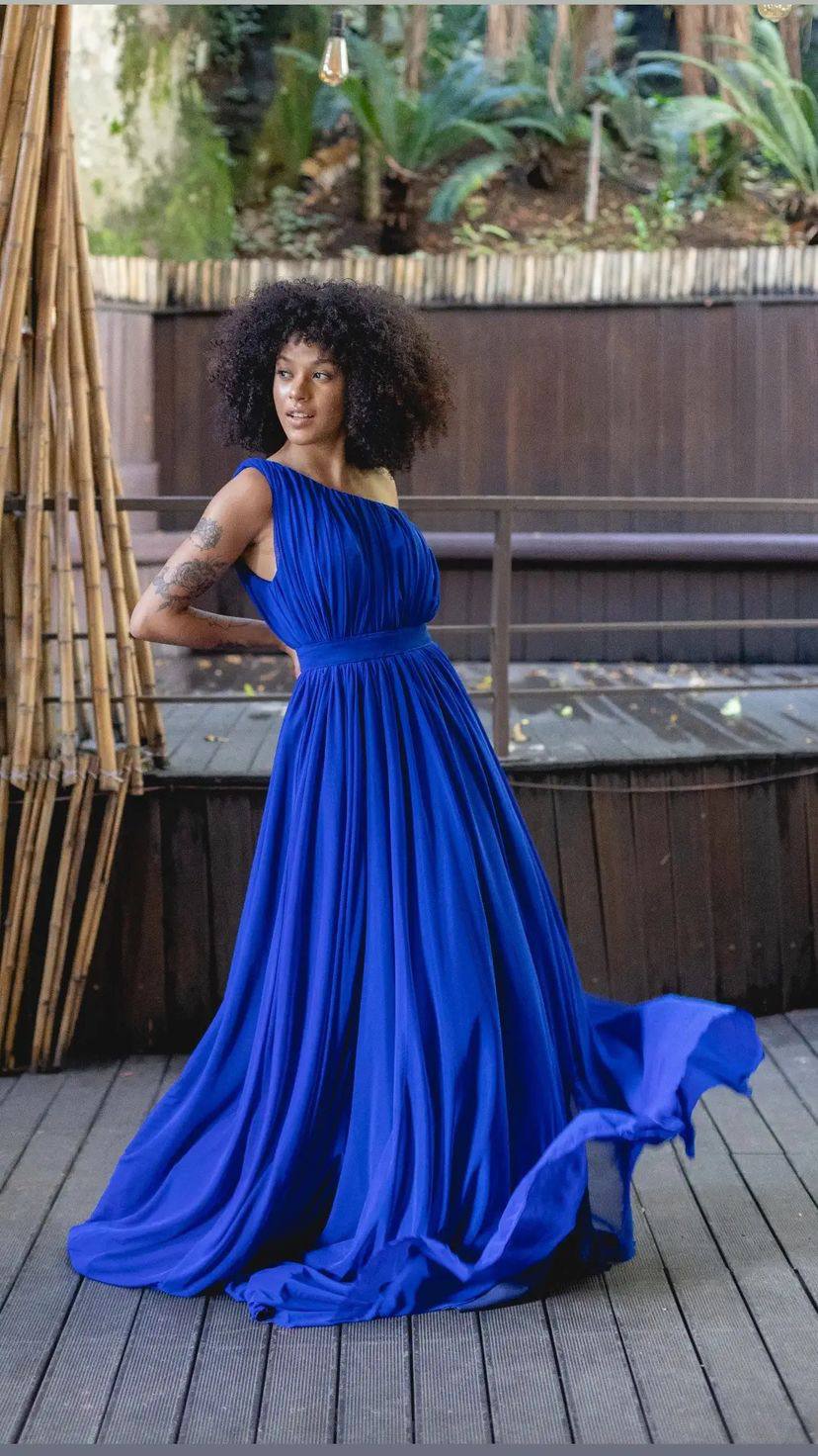 Vestido longo azul de um ombro, tecido leve e fluido, busto plissado e cintura marcada.