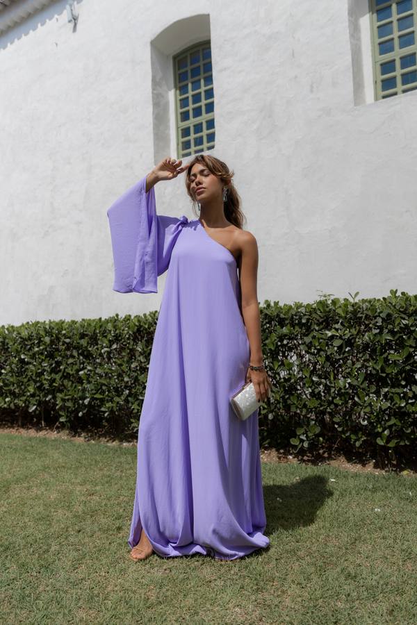 Vestido longo lilás de caimento fluido, modelagem um ombro com manga ampla e caimento leve.