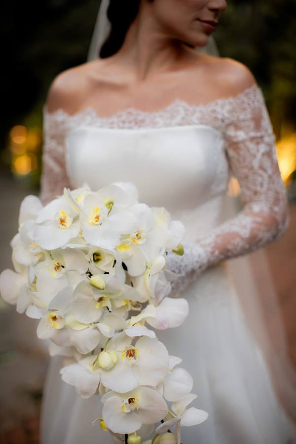 Vestido de noiva off-white de manga longa em renda, com buquê de orquídeas