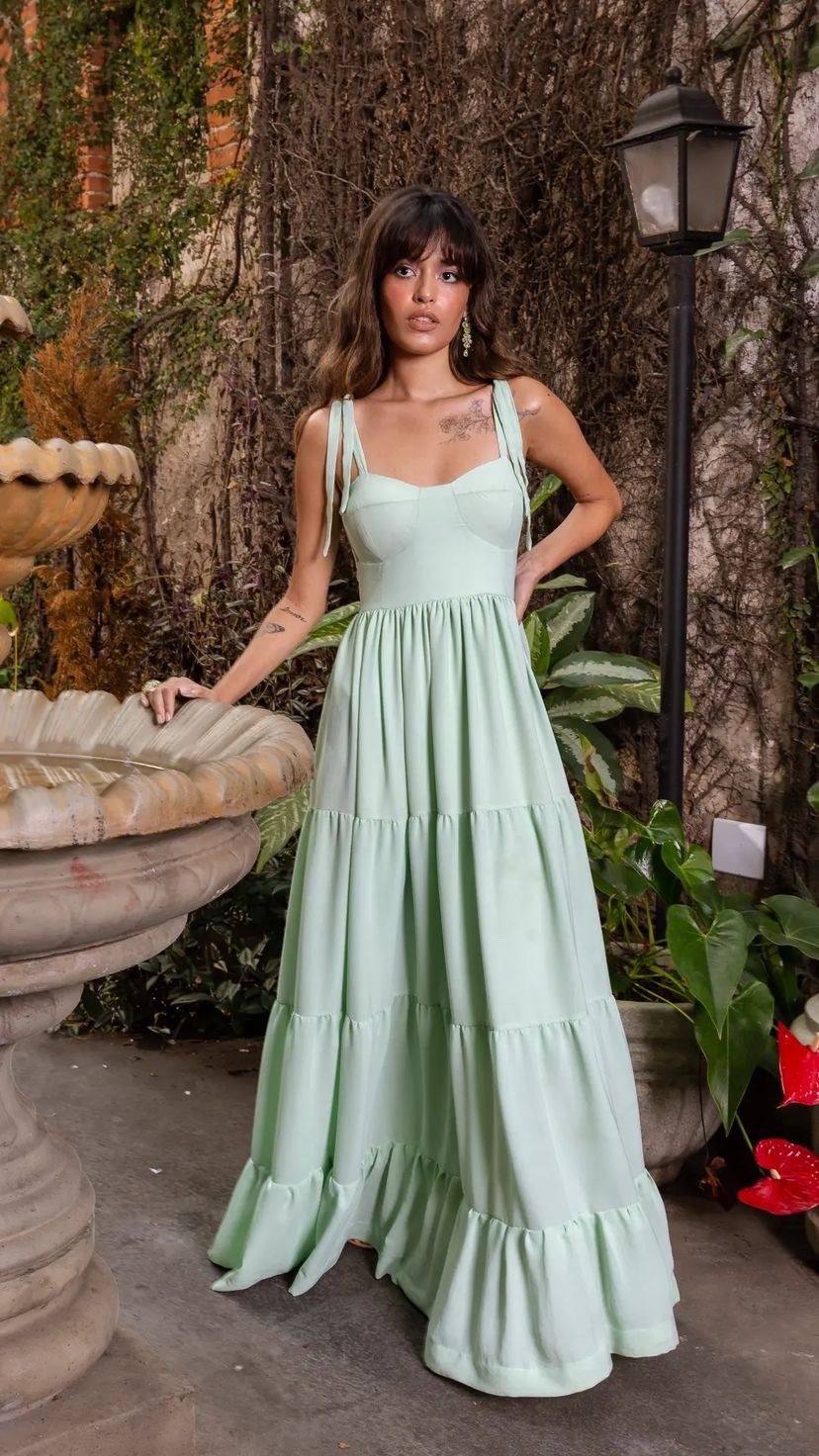 Vestido longo verde claro em tecido leve, com alças finas de amarração, corpo estruturado e saia ampla em camadas.