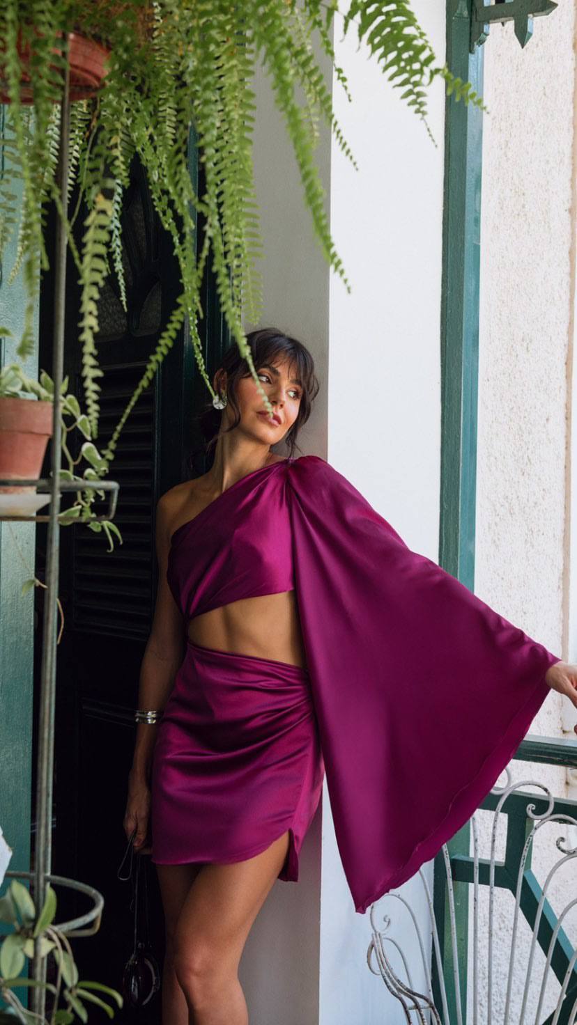 Vestido curto fúcsia de cetim com decote de um ombro, manga ampla drapeada e recorte na cintura.