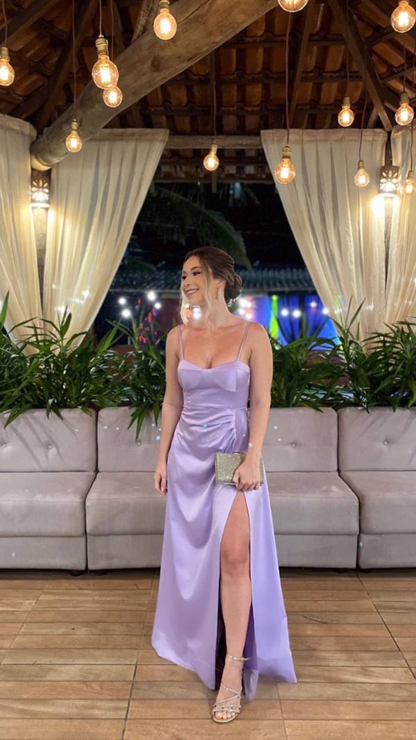 Vestido longo lilás em cetim, de alças finas, fenda profunda na saia e caimento fluido.