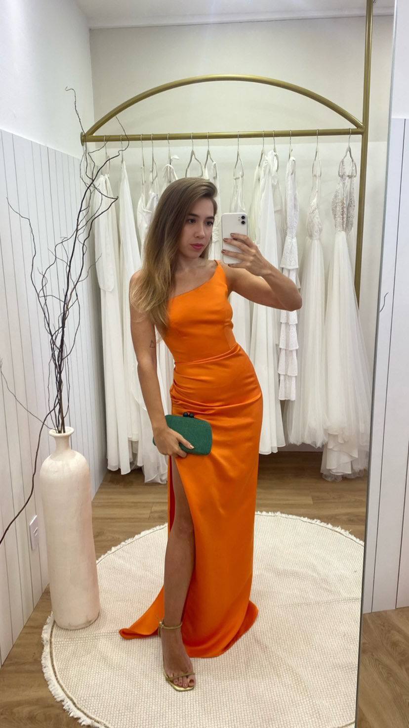 Vestido longo laranja de cetim, decote de um ombro só, caimento ajustado com drapeado e fenda lateral.