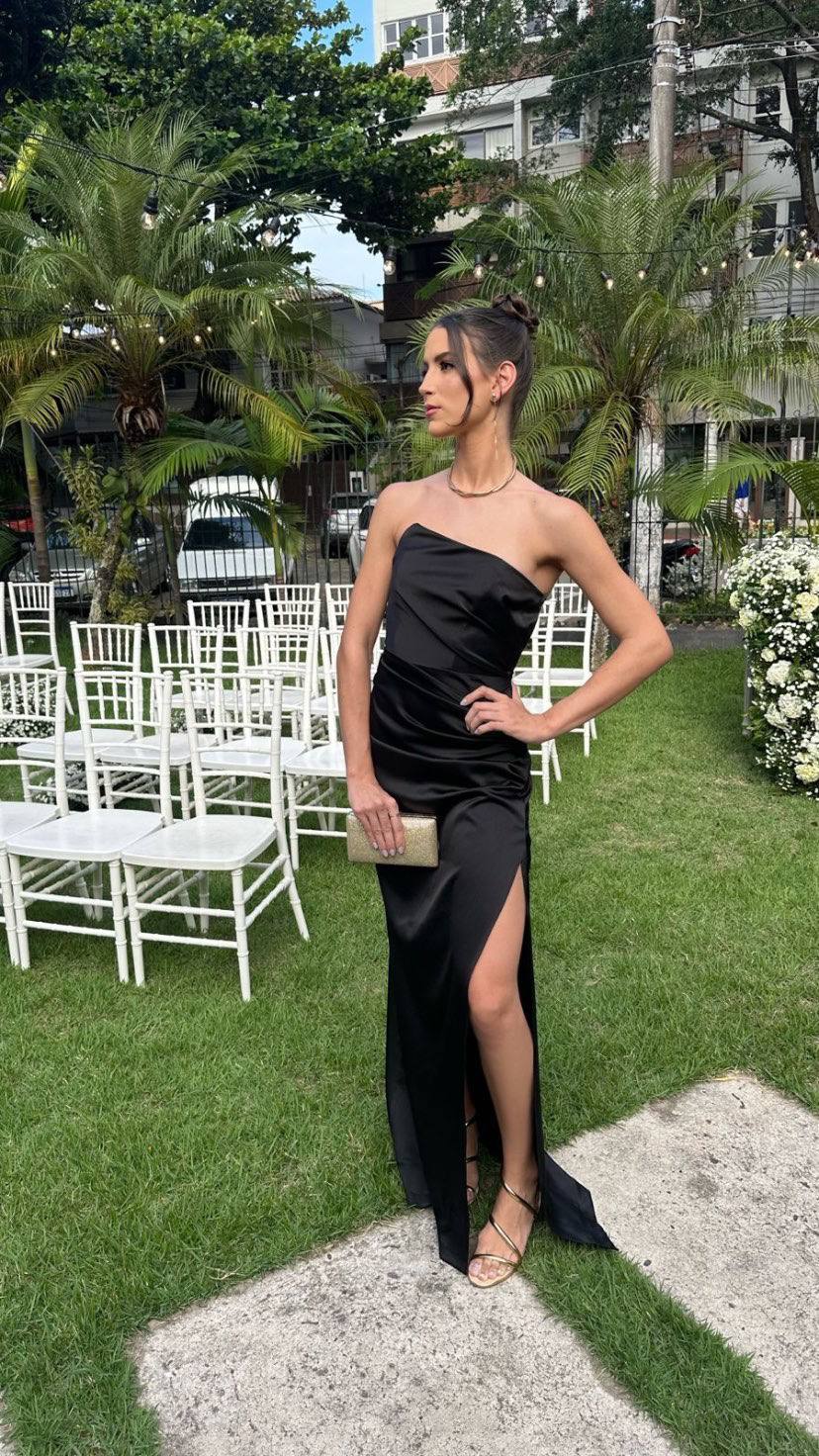 Vestido longo preto de cetim, tomara que caia, com modelagem ajustada, drapeado na cintura e fenda lateral.
