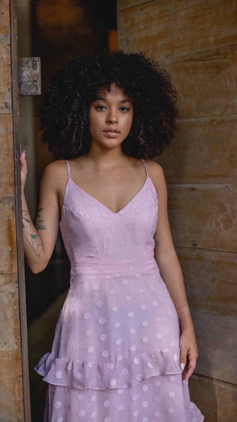 Vestido lilás de alça fina com decote V, padronagem de poás, cintura marcada e saia evasê com babados.