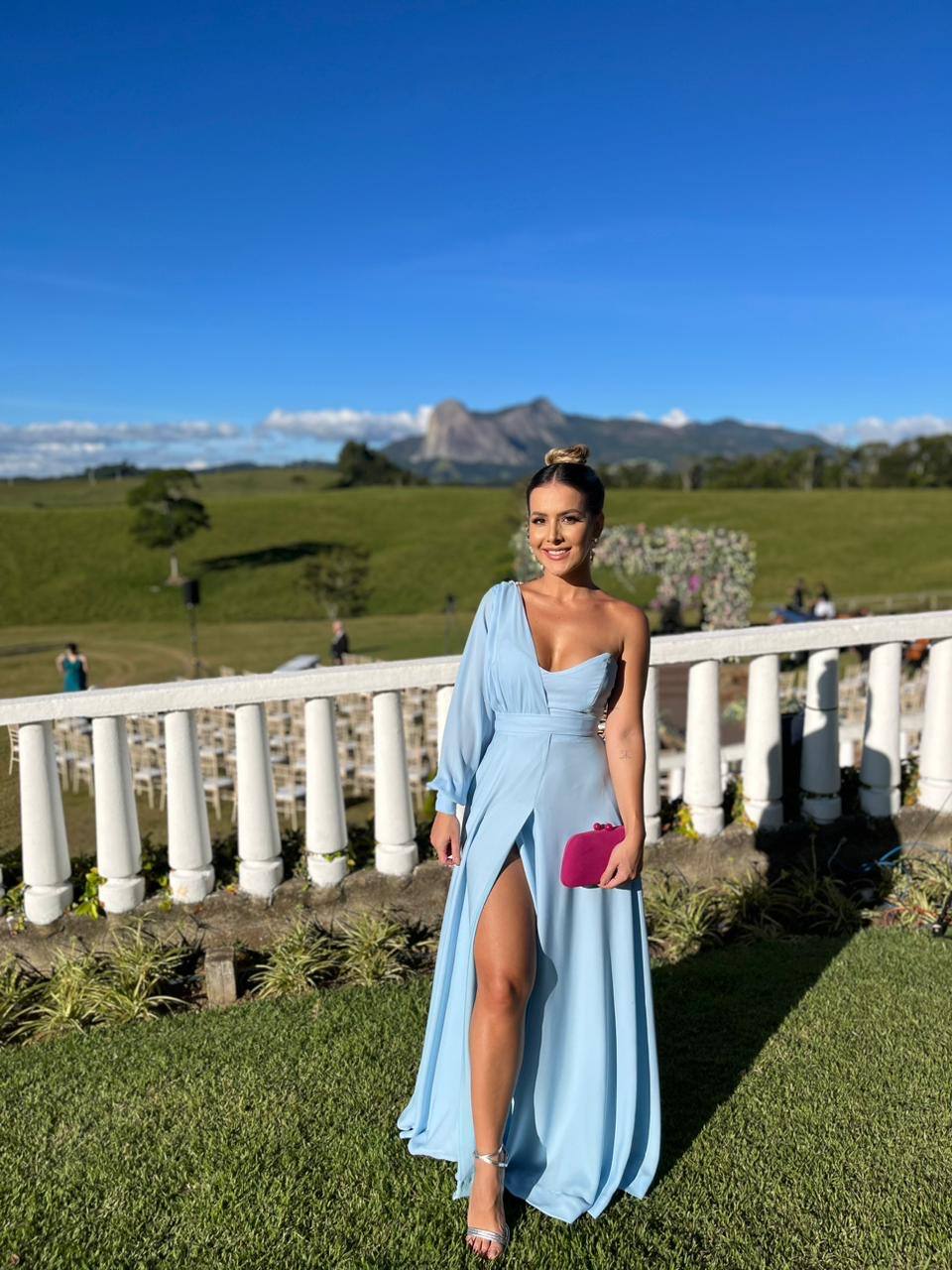 Vestido longo azul claro de um ombro só com manga longa, saia fluida e fenda frontal.
