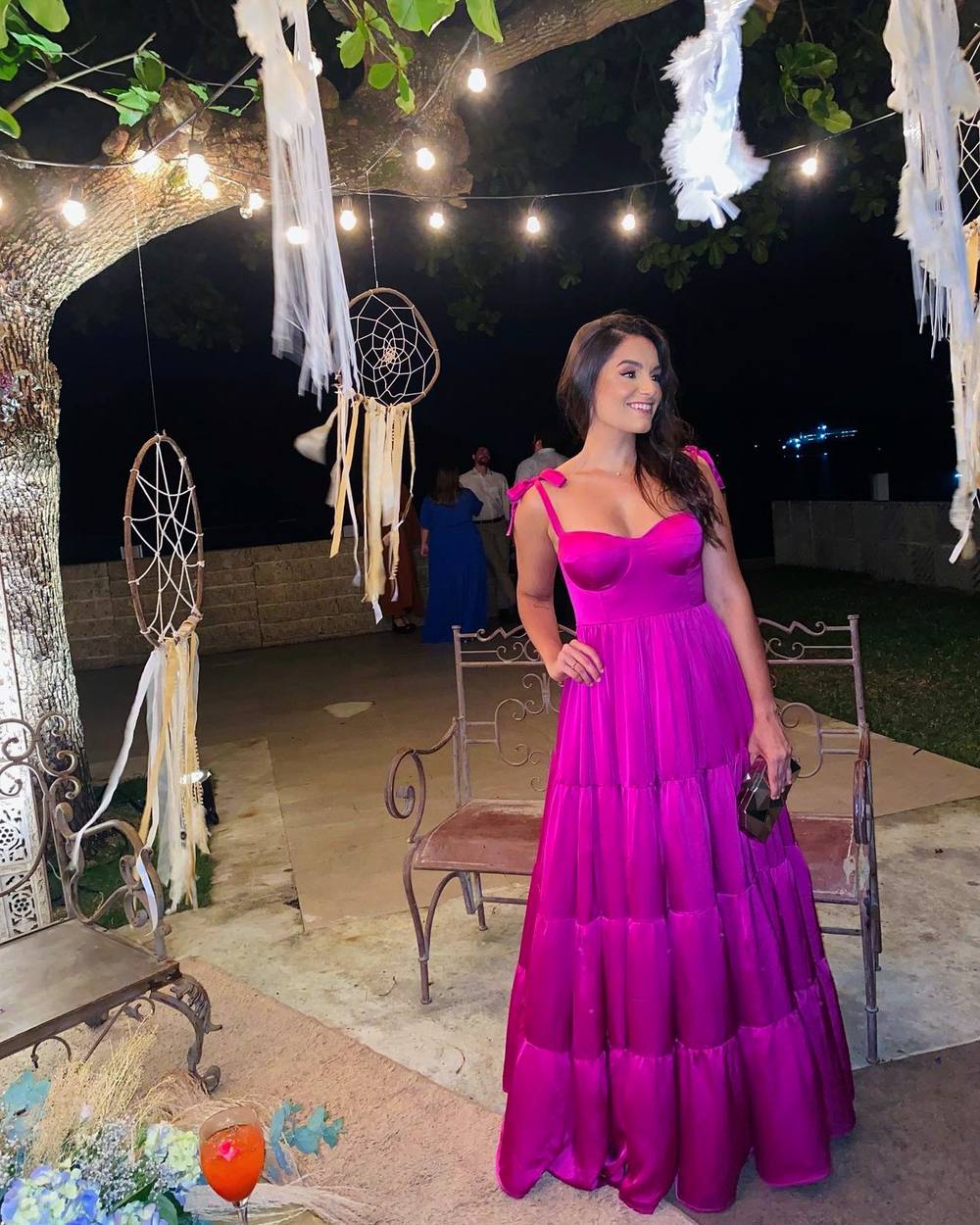 Vestido longo fúcsia com alças finas de laço, busto estruturado estilo corselet e saia em camadas.