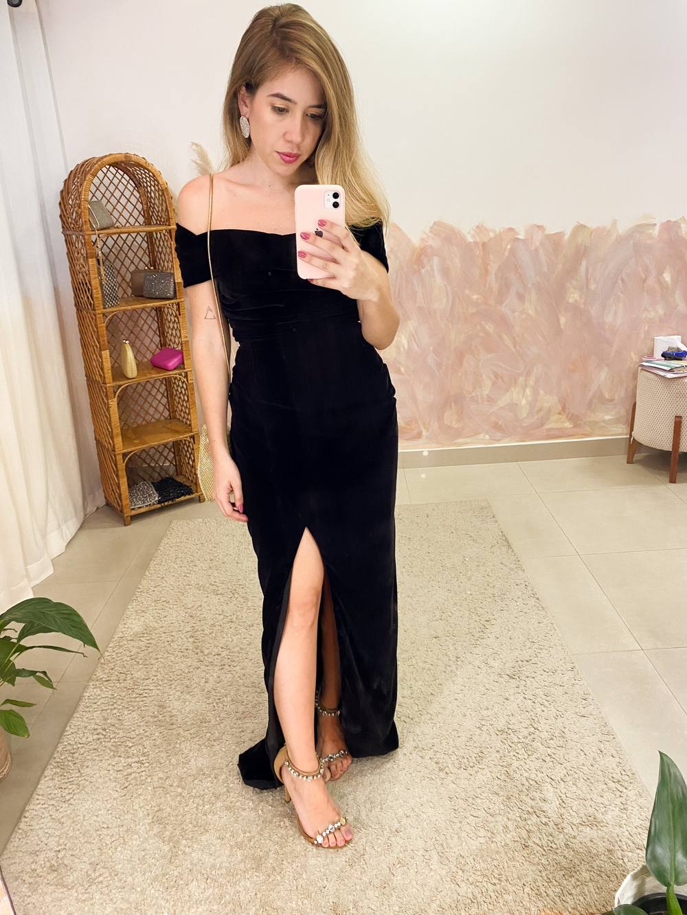 Vestido longo preto em veludo, decote ombro a ombro, caimento reto e fenda frontal.