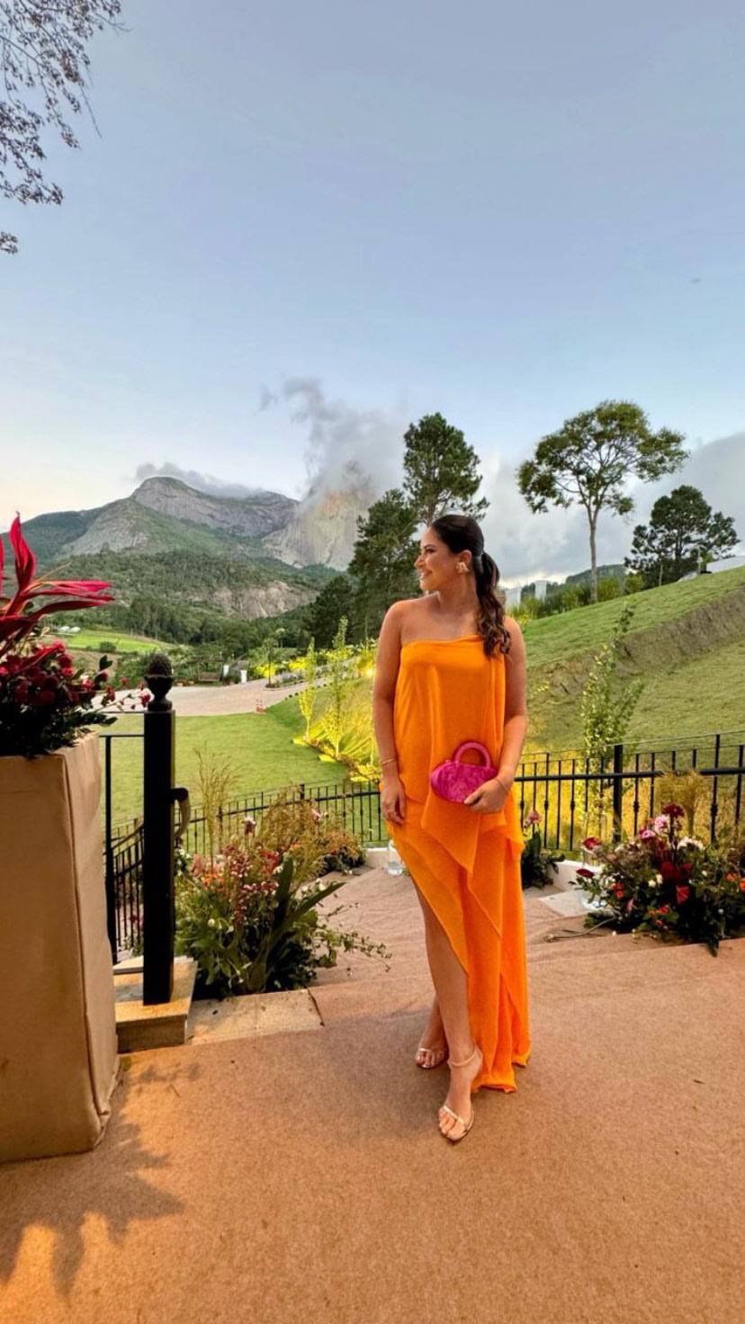 Vestido longo laranja de caimento fluido, modelo tomara que caia com saia assimétrica e fenda lateral.