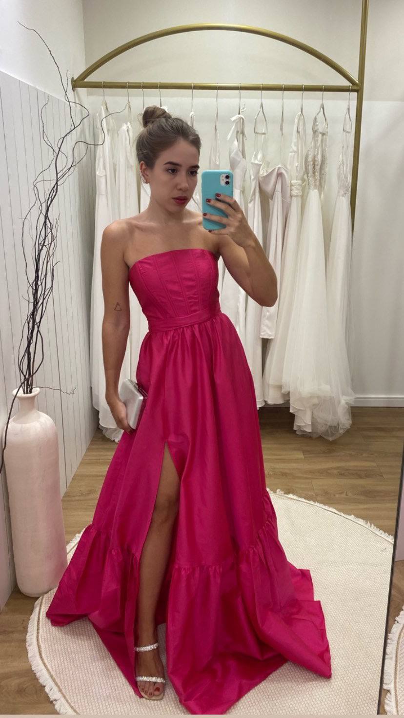 Vestido longo fúcsia tomara que caia, com corpo estruturado, saia ampla evasê e fenda frontal destacada.