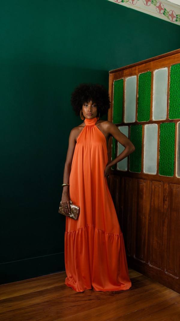 Vestido longo laranja de caimento fluido, decote frente única com gola alta e saia ampla com babado na barra.