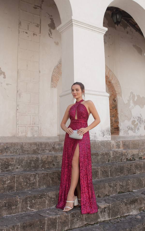 Vestido longo fúcsia de paetês, com decote frente única cruzado, fenda frontal e caimento ajustado.