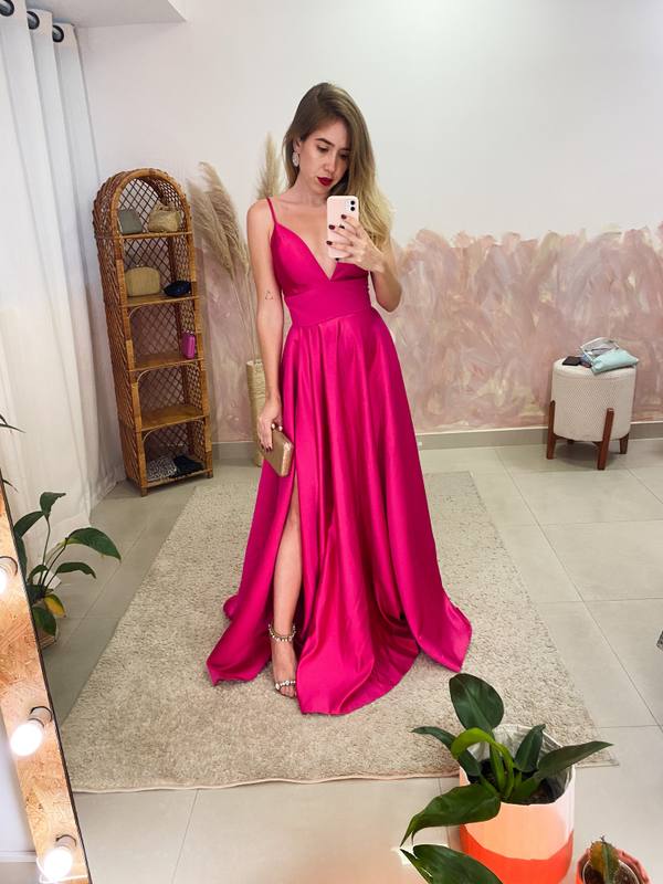 Vestido longo fúcsia em cetim, com decote V, alças finas, saia ampla evasê e fenda lateral.
