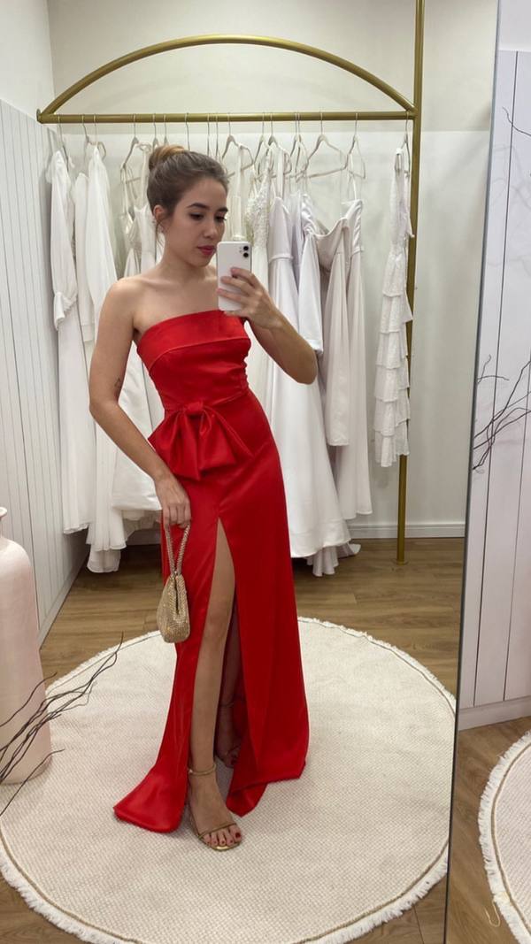 Vestido longo vermelho de cetim, decote tomara que caia, com laço na cintura e fenda frontal pronunciada.