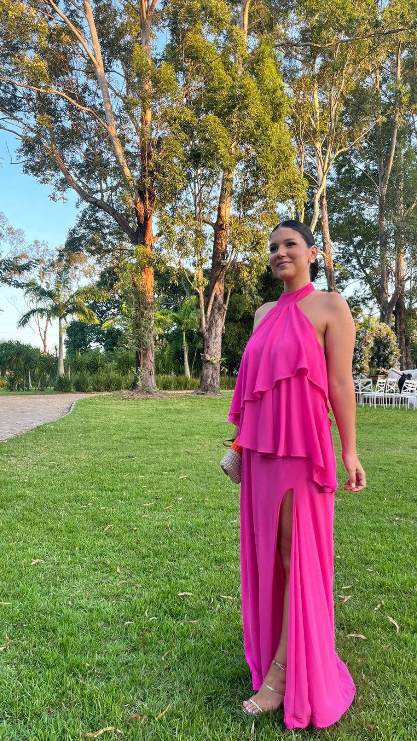 Vestido longo fúcsia fluido de frente única, com babados sobrepostos no busto e fenda lateral na saia.