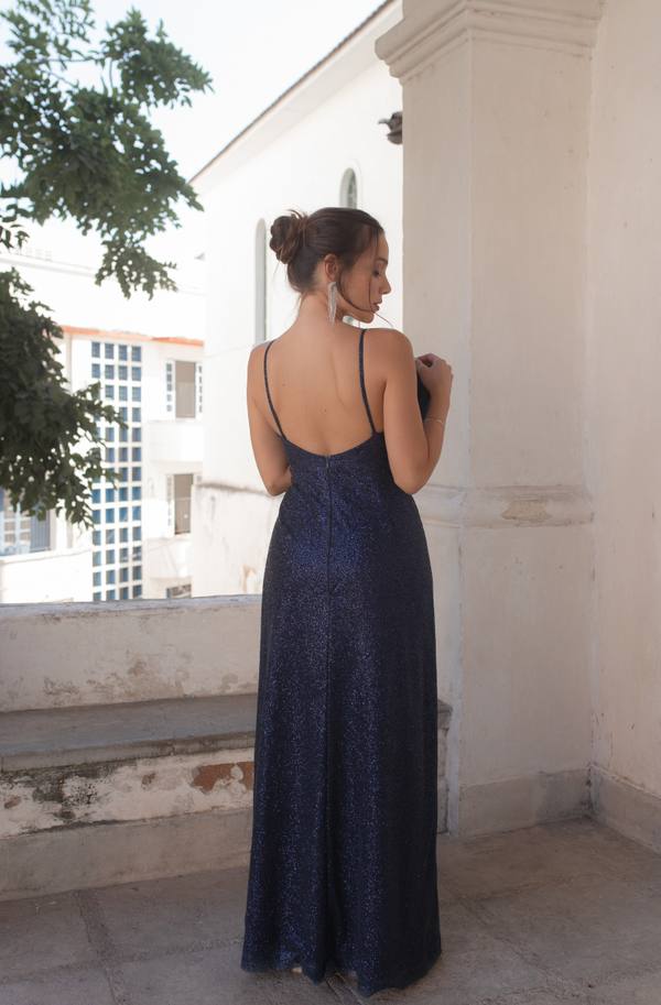 Vestido longo azul escuro de brilho com alças finas, decote baixo nas costas e caimento reto.