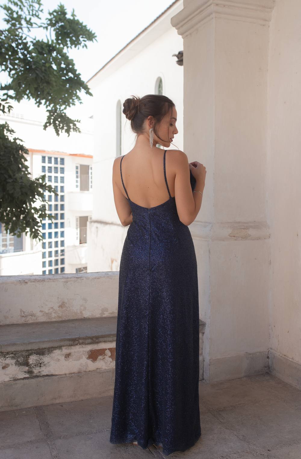 Vestido longo azul escuro de brilho com alças finas, decote baixo nas costas e caimento reto.