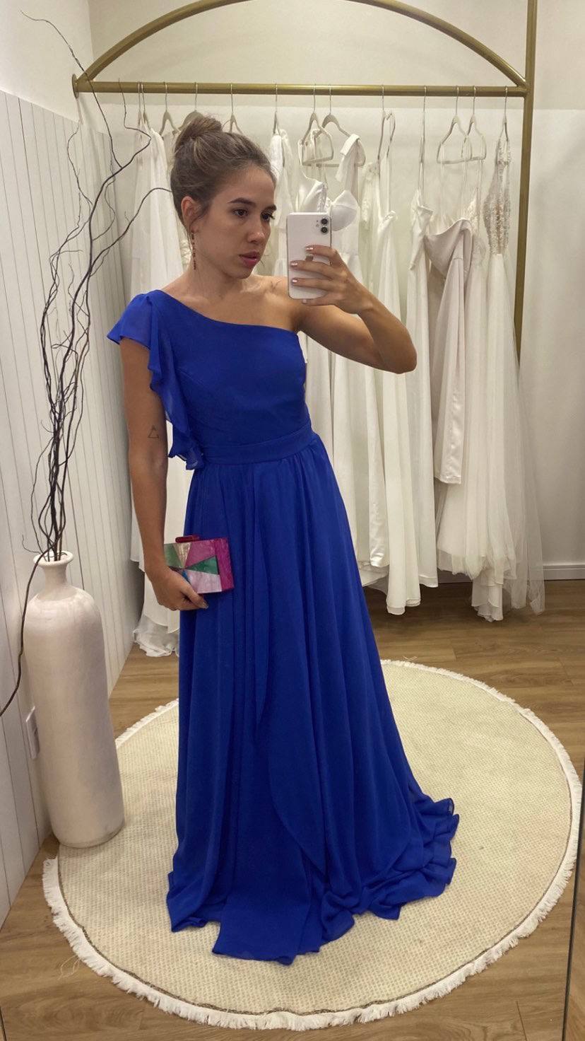 Vestido longo azul de tecido fluido, modelo um ombro com detalhe de babado e saia leve.