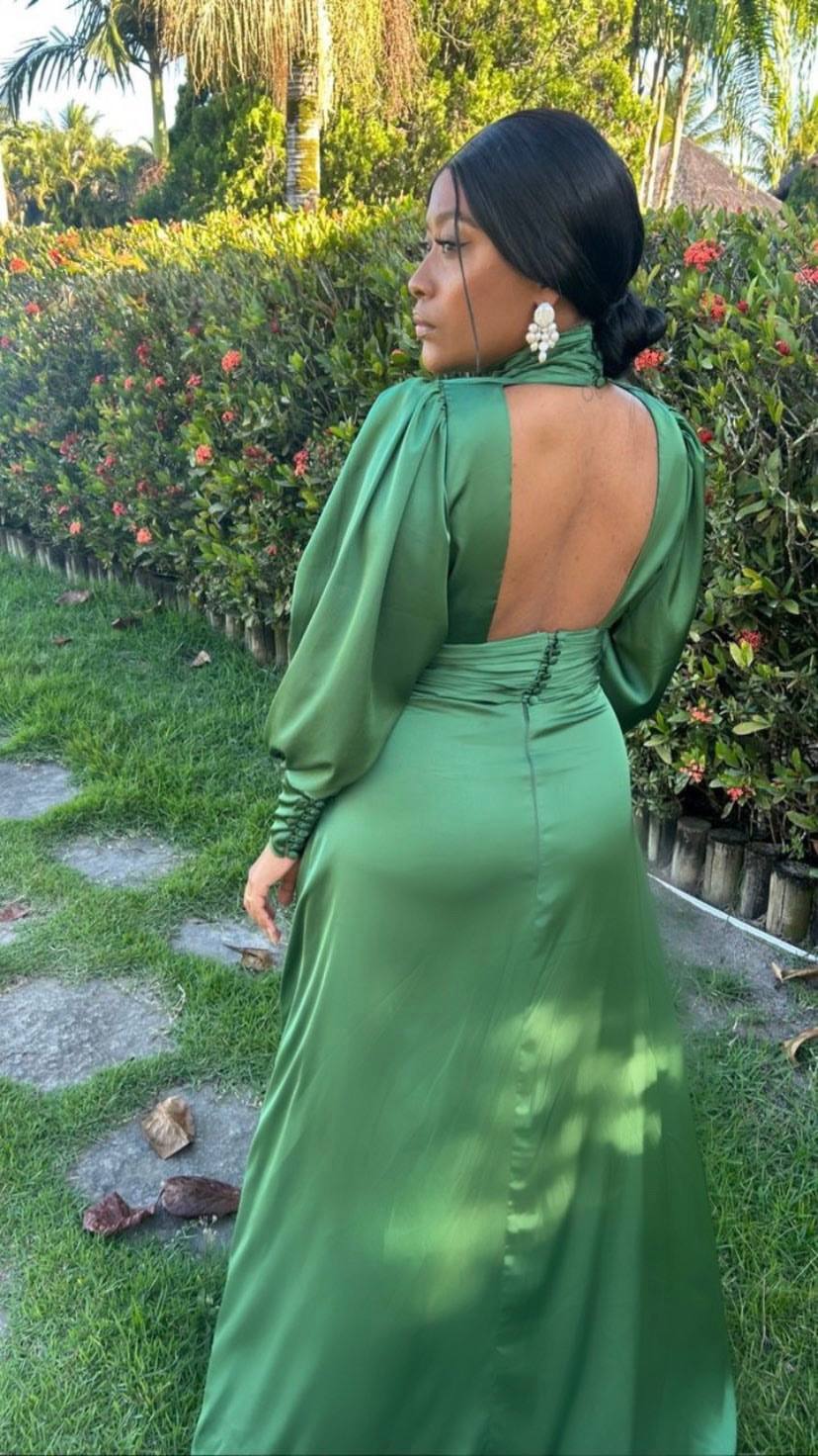 Vestido longo verde de cetim com mangas longas, decote aberto nas costas e saia fluida.