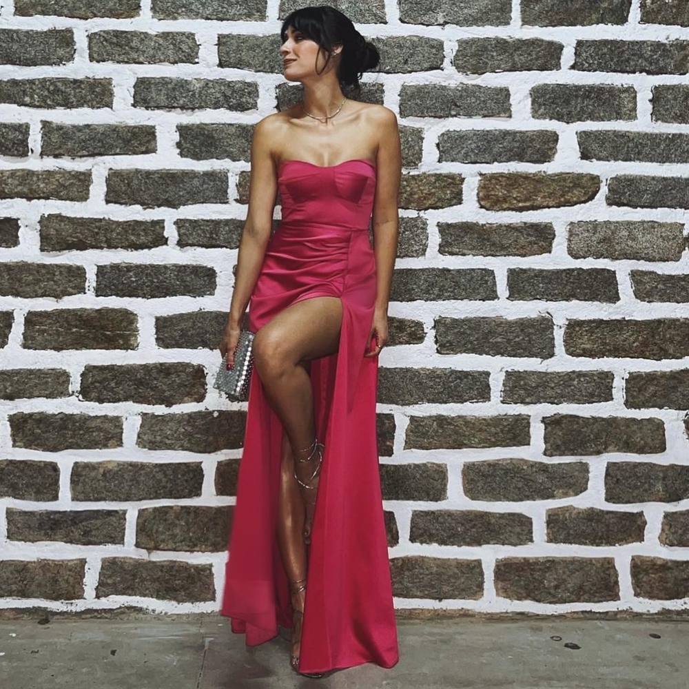 Vestido longo fúcsia tomara que caia em cetim, com caimento fluido, drapeado no quadril e fenda profunda na saia.