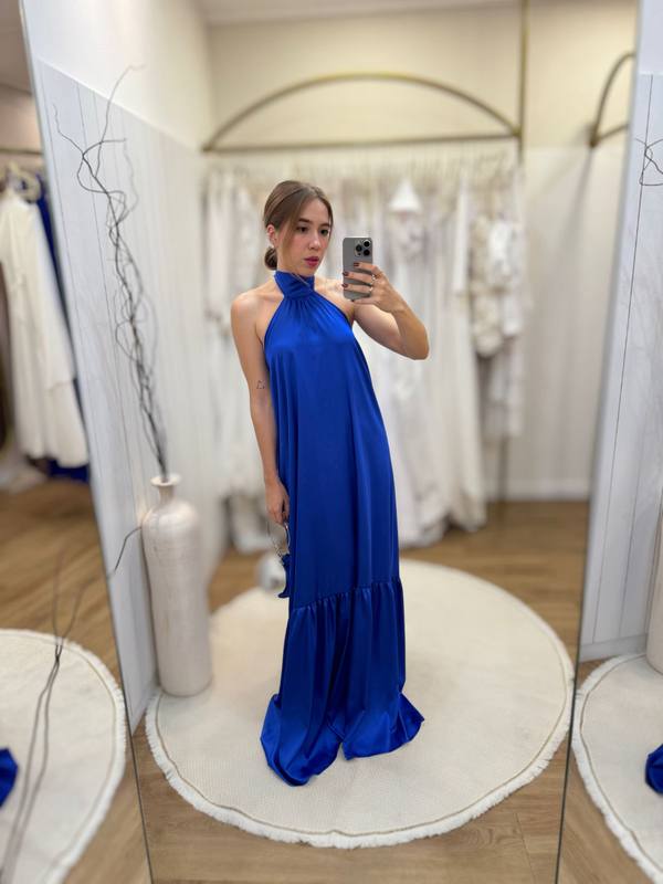 Vestido longo azul de cetim, com decote frente única, caimento fluido e babado no barrado.