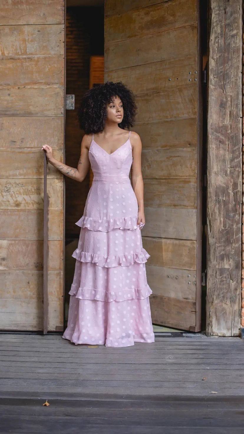 Vestido longo rosé com alças finas, decote em V, textura poá e saia fluida em camadas com babados.