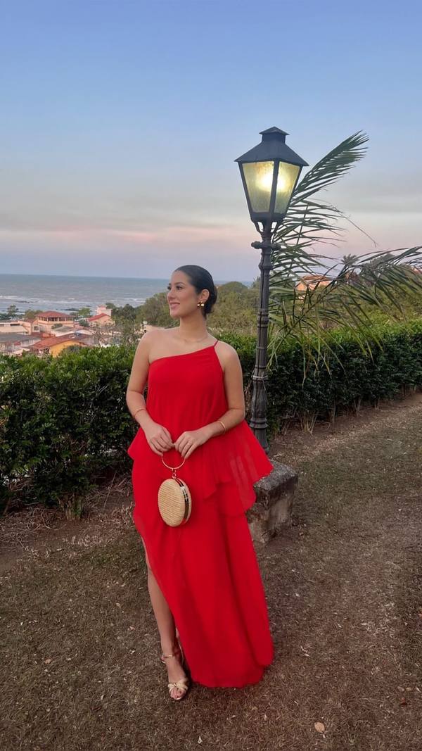 Vestido longo vermelho de um ombro só, em tecido fluido com camadas, caimento leve e fenda lateral.