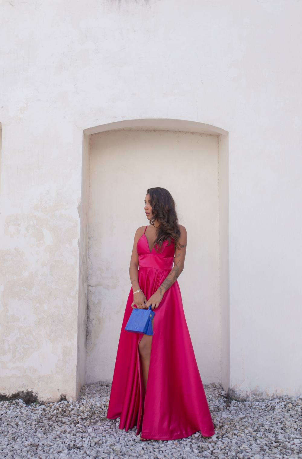 Vestido longo fúcsia de cetim com alças finas, decote V, fenda na saia e caimento evasê.