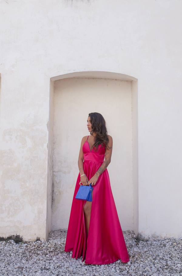 Vestido longo fúcsia de cetim com alças finas, decote V, fenda na saia e caimento evasê.