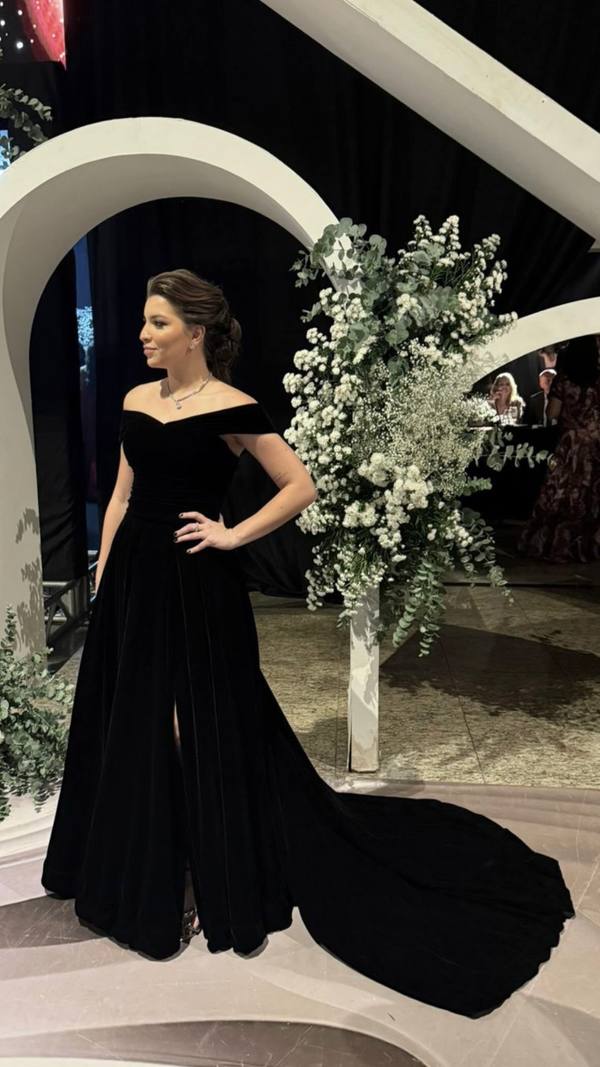 Vestido longo preto em veludo, com decote ombro a ombro, fenda frontal e saia evasê com cauda.