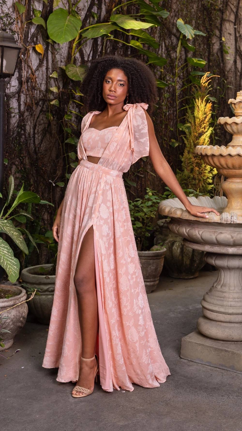 Vestido longo rosé em tecido fluido com fenda profunda na saia, recorte na cintura e laços nos ombros.