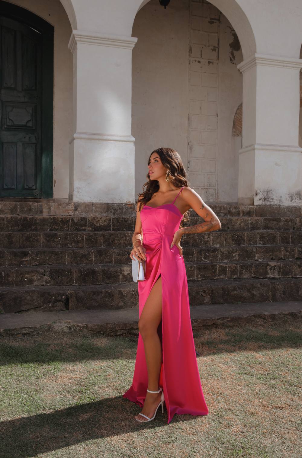 Vestido longo fúcsia de cetim, com alças finas, fenda frontal e caimento fluido.