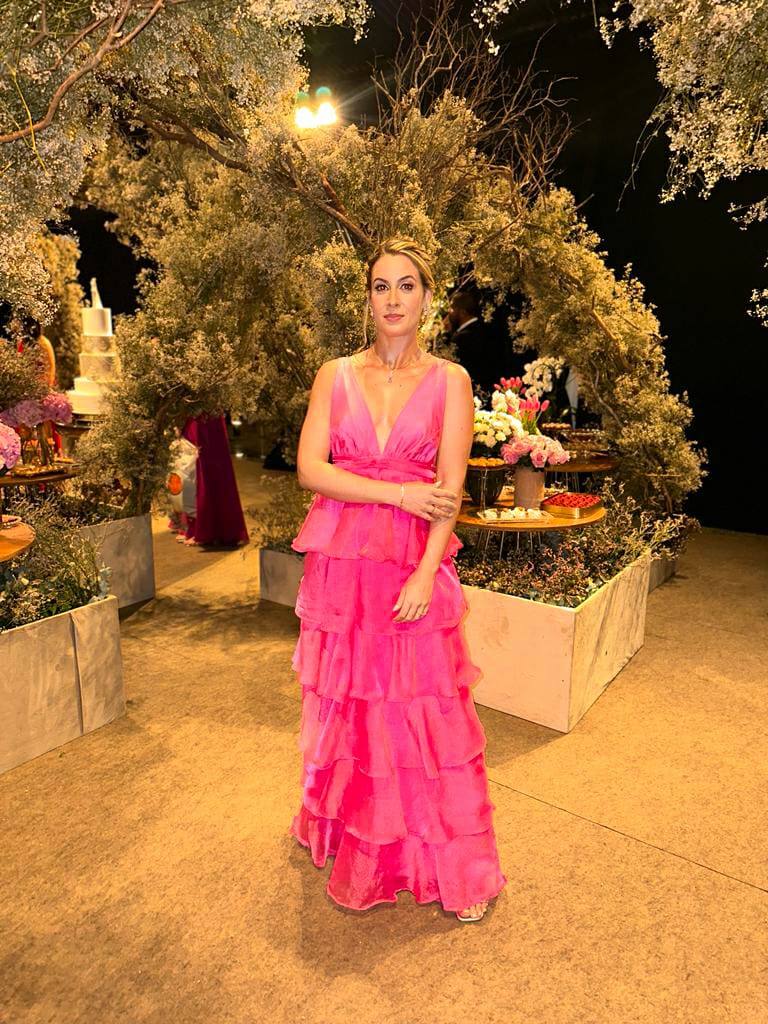 Vestido longo fúcsia com decote V profundo, saia fluida em camadas de babados e caimento leve.