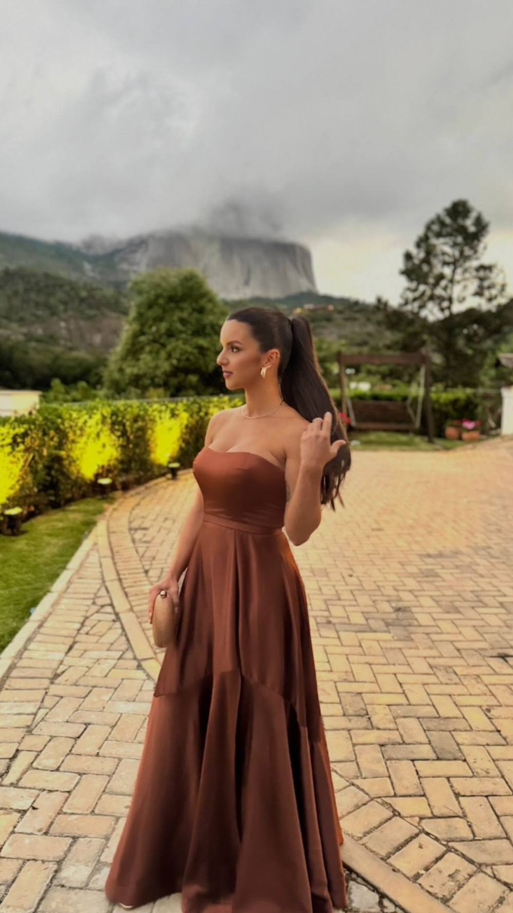 Vestido longo marrom de cetim, com decote tomara que caia, cintura marcada e saia ampla evasê.
