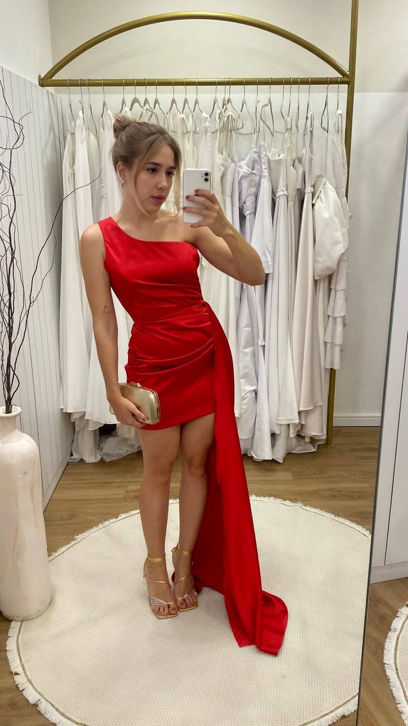 Vestido curto vermelho em tecido acetinado, modelo um ombro com drapeado e cauda lateral longa.