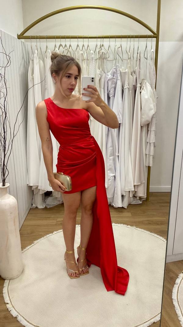 Vestido curto vermelho em tecido acetinado, modelo um ombro com drapeado e cauda lateral longa.