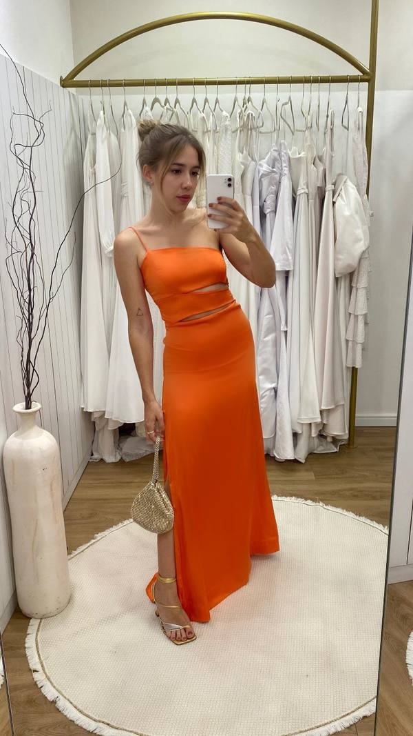 Vestido longo laranja de alça fina, com recortes vazados na cintura e saia reta com fenda lateral.