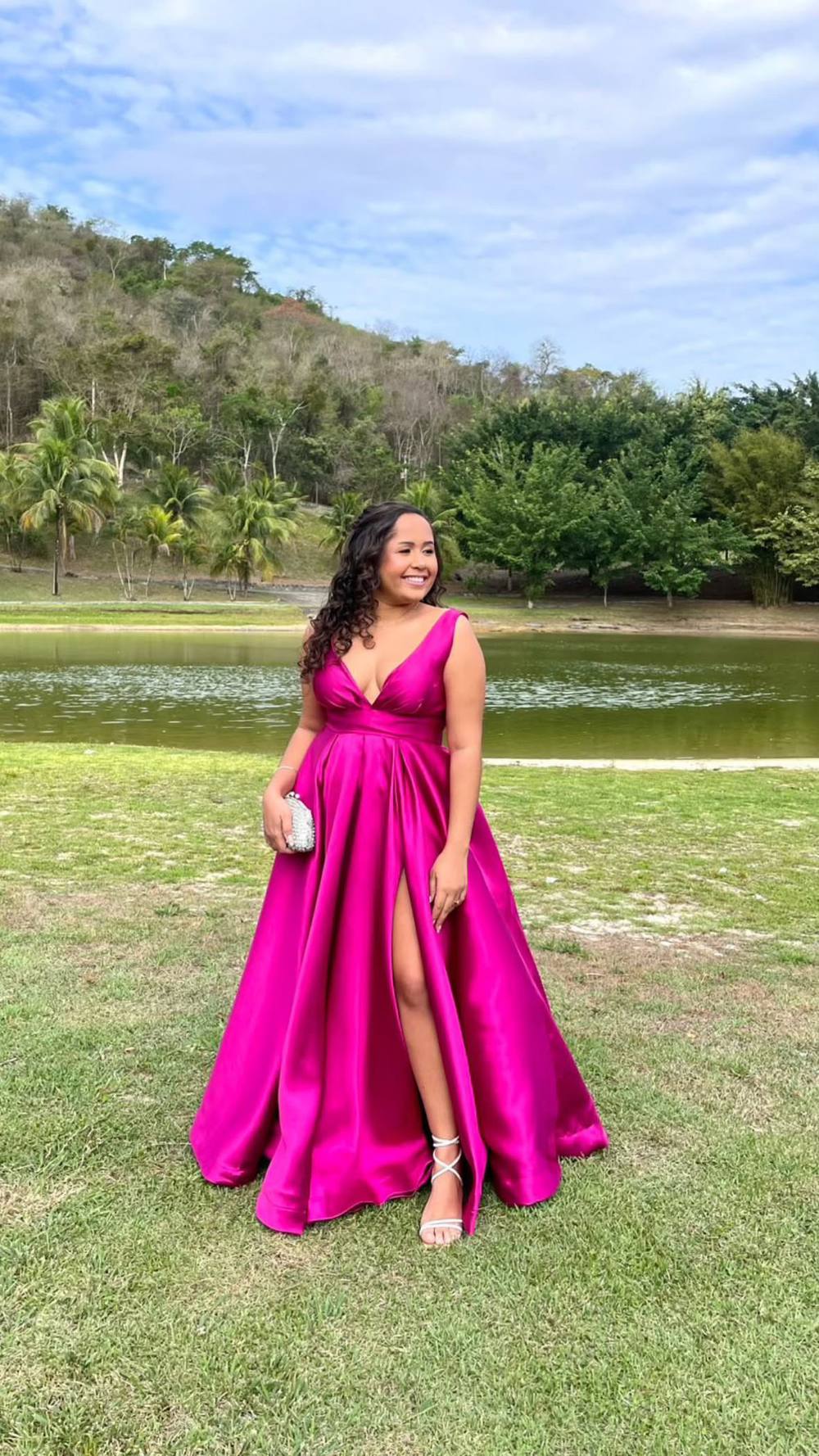 Vestido longo fúcsia em tecido acetinado, com decote V, saia ampla e fenda lateral em destaque.