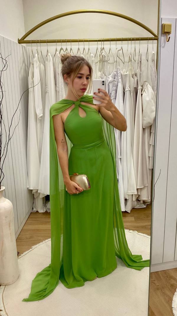 Vestido longo verde de tecido fluido, com decote frente única, detalhe de nó no pescoço e capa esvoaçante embutida.
