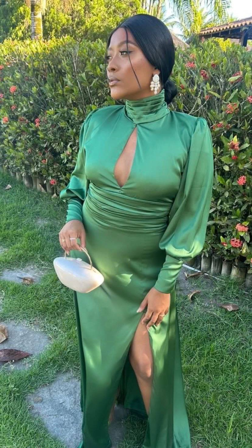 Vestido longo verde de cetim, com mangas longas, gola alta, recorte no decote e fenda frontal.